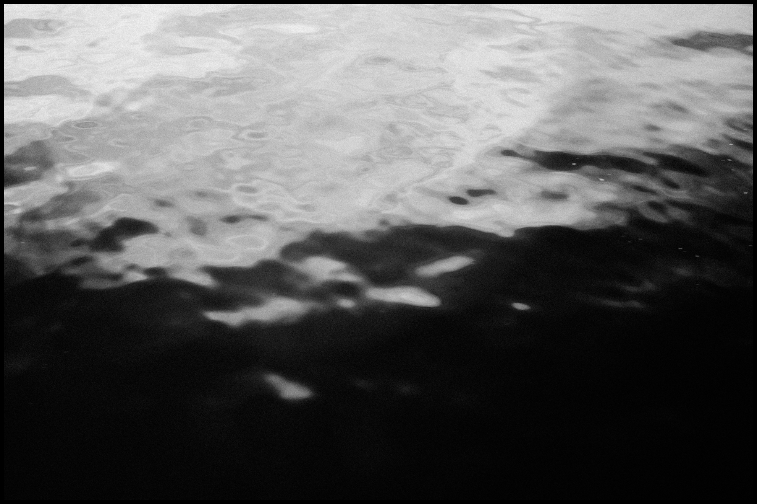 Black and white abstract image showing blurred, wavy patterns resembling light and shadow reflected on a water surface.