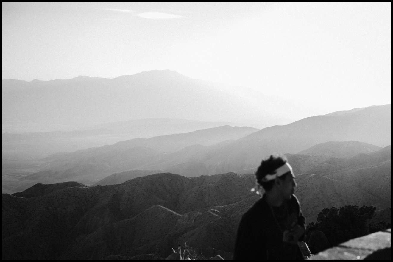 A person stands in the foreground with blurred mountains and a hazy sky in the background, captured in black and white.